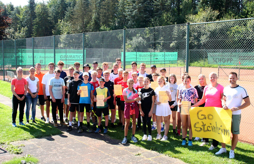 Eine große Gruppe von ca. 40 Spielern und Spielerinnen sowie Lehrkräften stehen vor einem Tennisplatz in Bad Driburg.