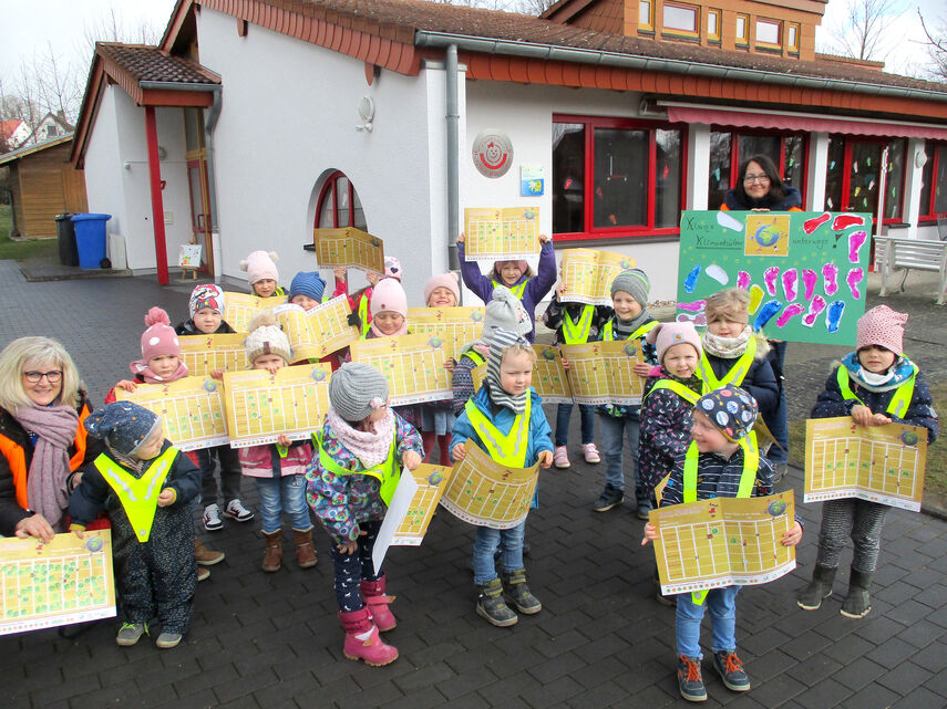 Vorschlag hier: Im Bewegungskindergarten „Kinderlobby“ in Warburg-Menne halten mehrere Kinder und 2 Erzieherinnen den Stundenplan der Kindermeilen-Aktion in die Höhe.