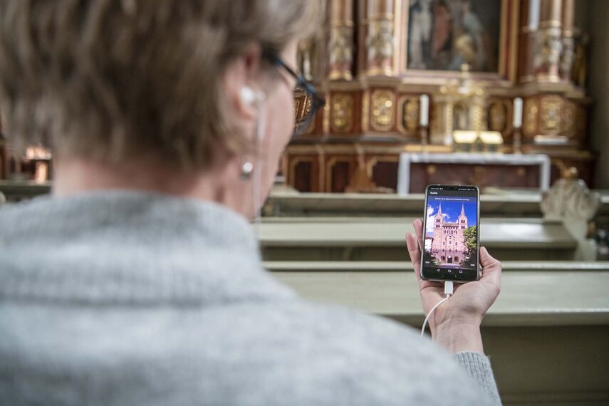 Eine Dame nutzt innerhalb der Corveyer Kirche eine App per Smartphone, um sich eine von acht Hörgeschichten anzuhören.